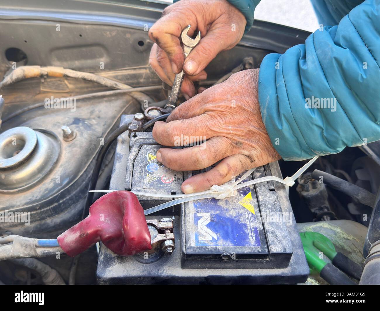 Man's hands trying to remove a damaged car battery using tools, such as wrenches Stock Photo