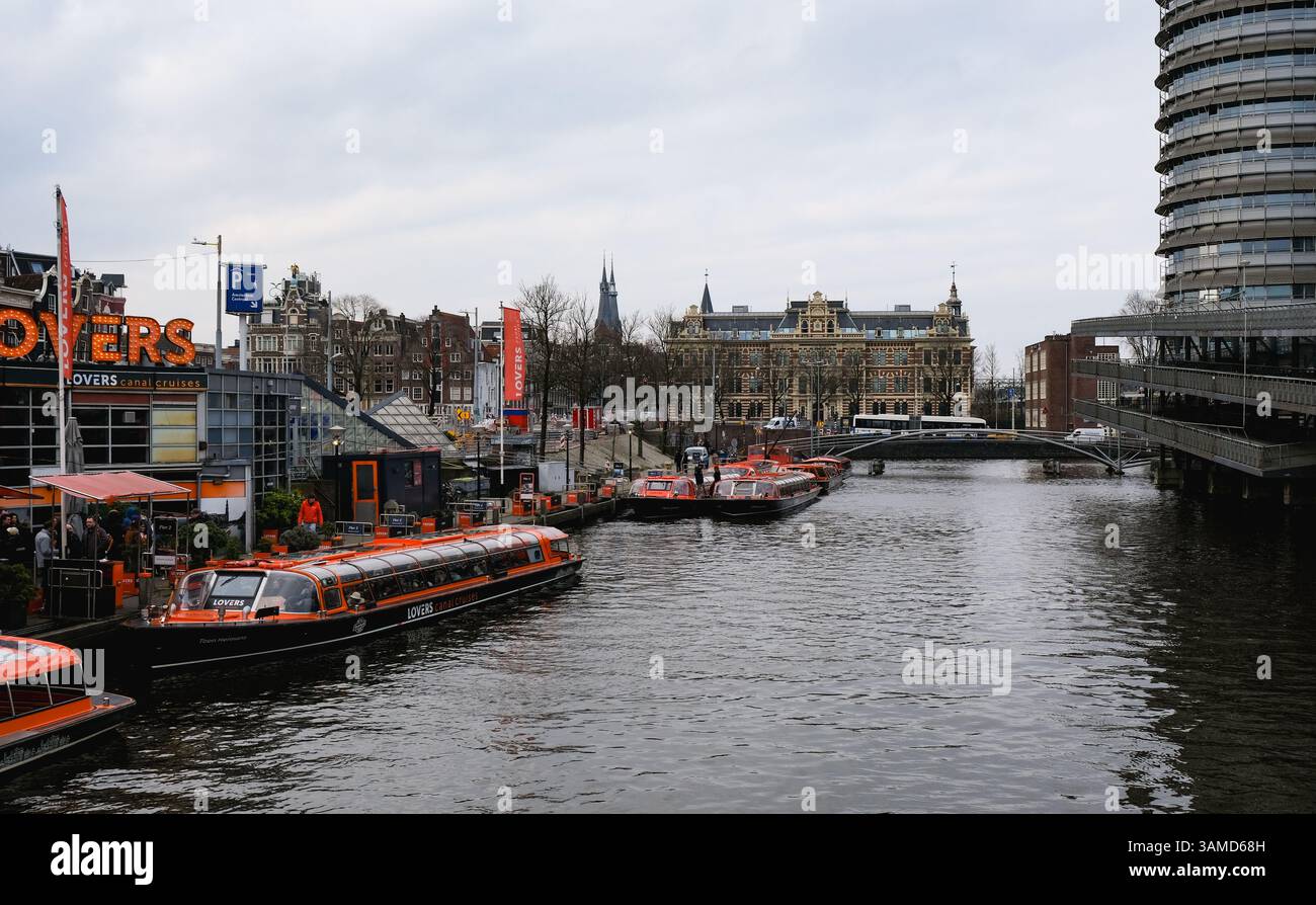 Amsterdam Netherlands, February 14 2025: Orange lovers canal cruises boats embarking tourists in amsterdam canal with typical dutch houses in the back Stock Photo