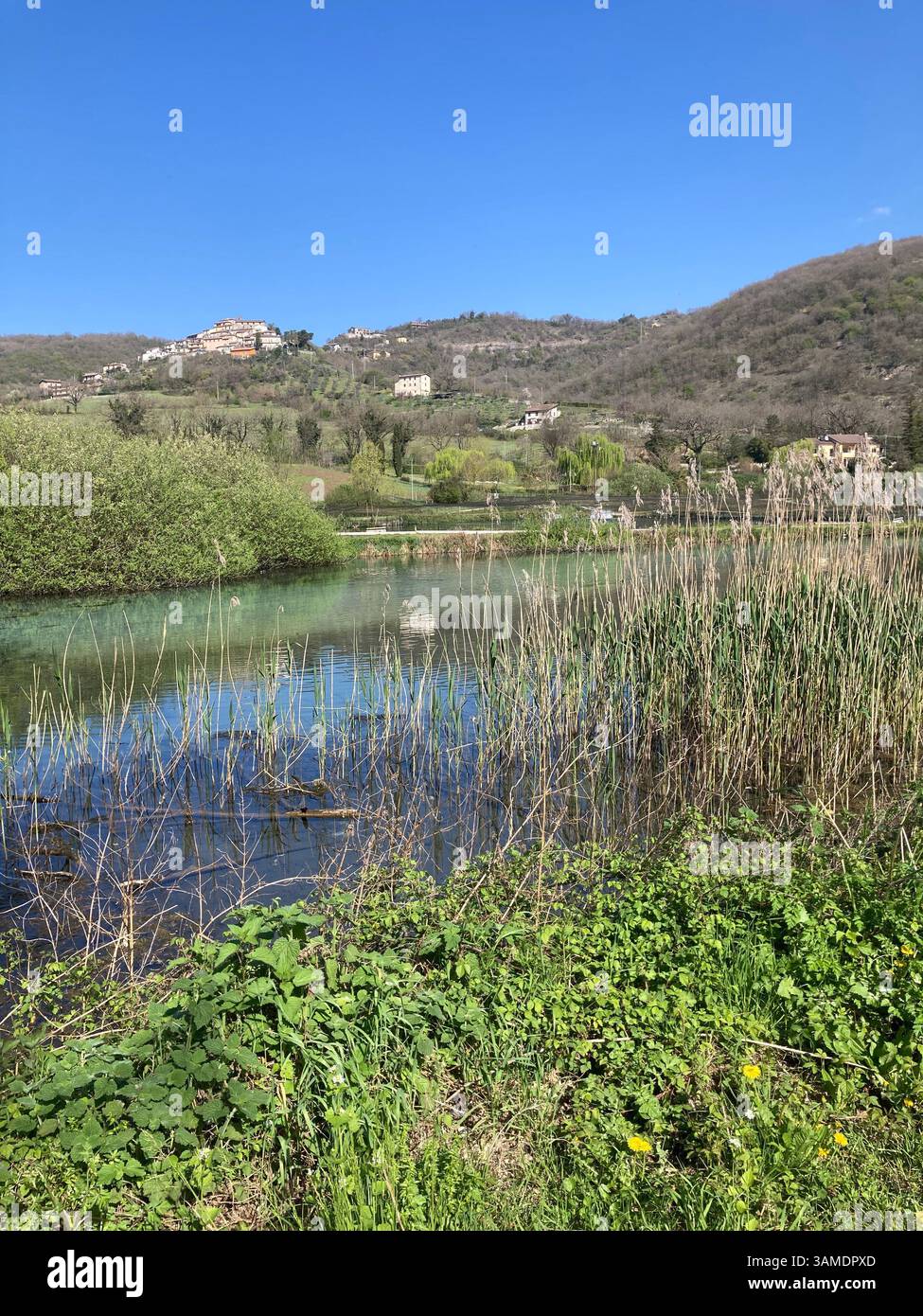 SPLENDIDA ORGENTE DI ACQUA CRISTALLINA CIRCONDATA DA VEGETAZIONE E CASE IN LONTANANZA CON UN IELO STUPENDO - Smartphone Captured Stock Image