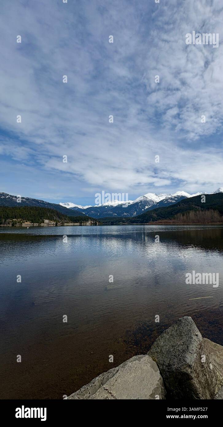 Snowy Mountain Range Reflected in Quiet Lake with Rocky Shoreline - Smartphone Captured Stock Image