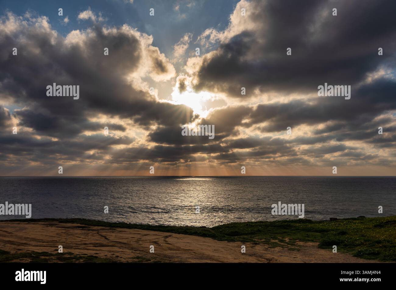 Golden sunlight breaks through dark clouds over the ocean, casting rays ...