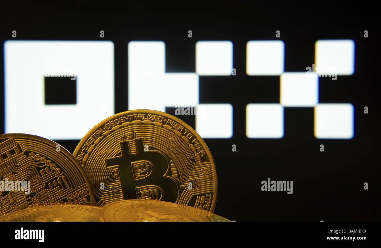 Close-up of Bitcoin coins with the OKX logo visible on a screen in the background Stock Photo