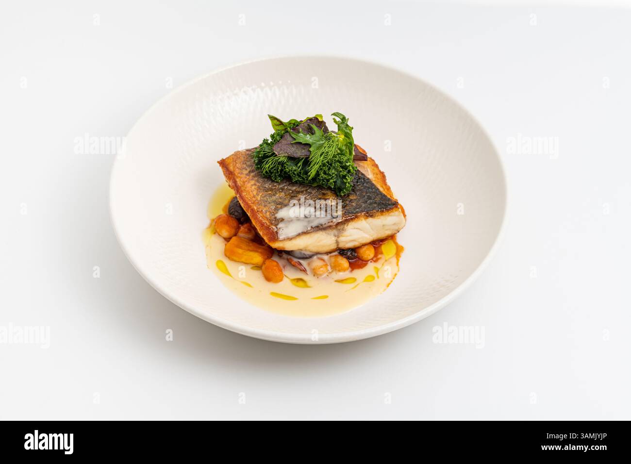 Crispy-skinned pan-seared fish fillet with chickpeas, creamy sauce, and fresh greens Stock Photo