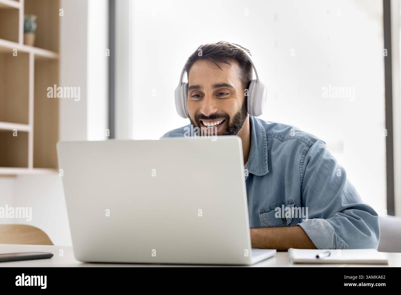 Smiling young man wear wireless headset communicate online using notebook Stock Photo
