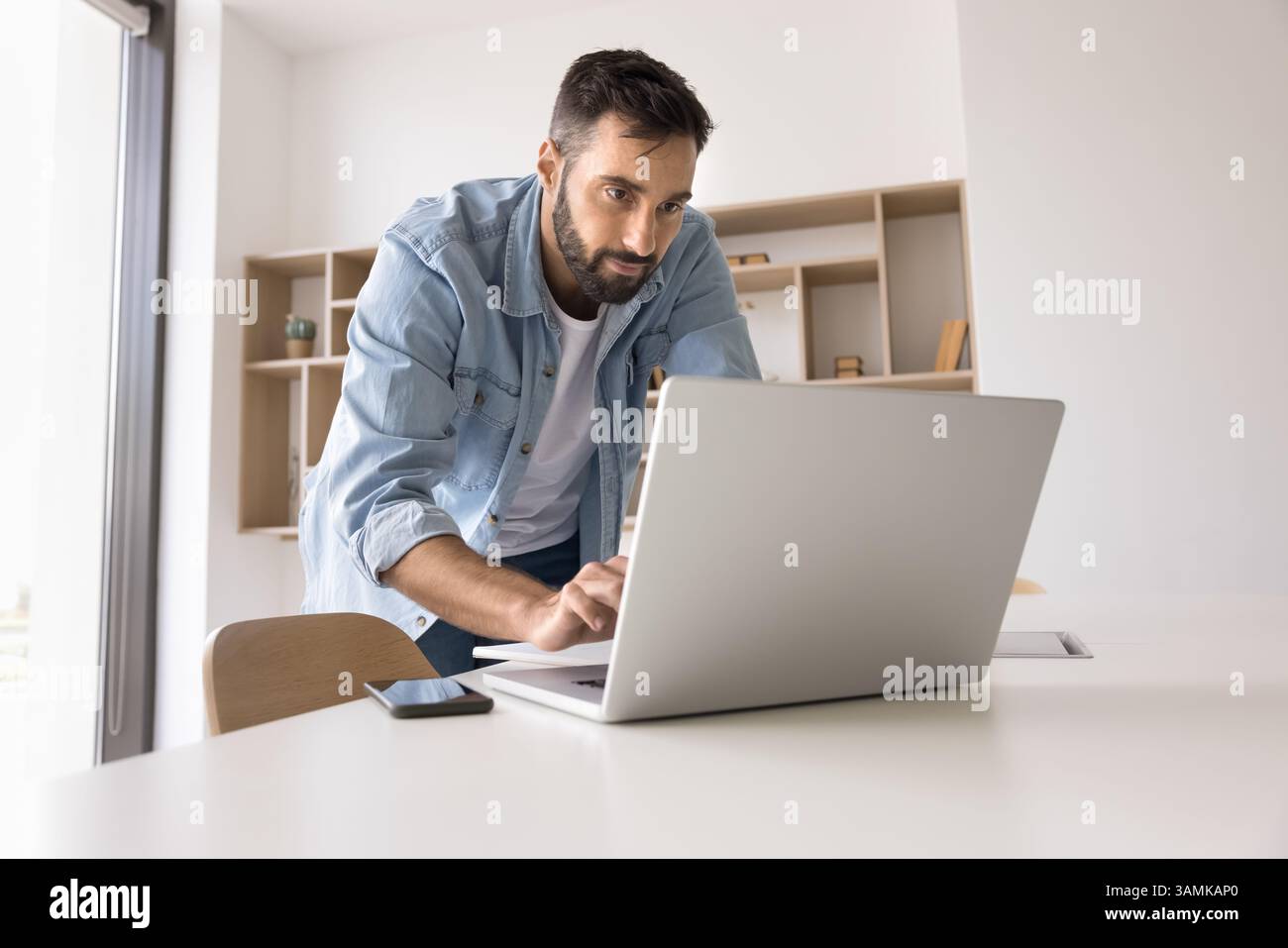 Concentrated young man leaning over work desk type on notebook Stock Photo