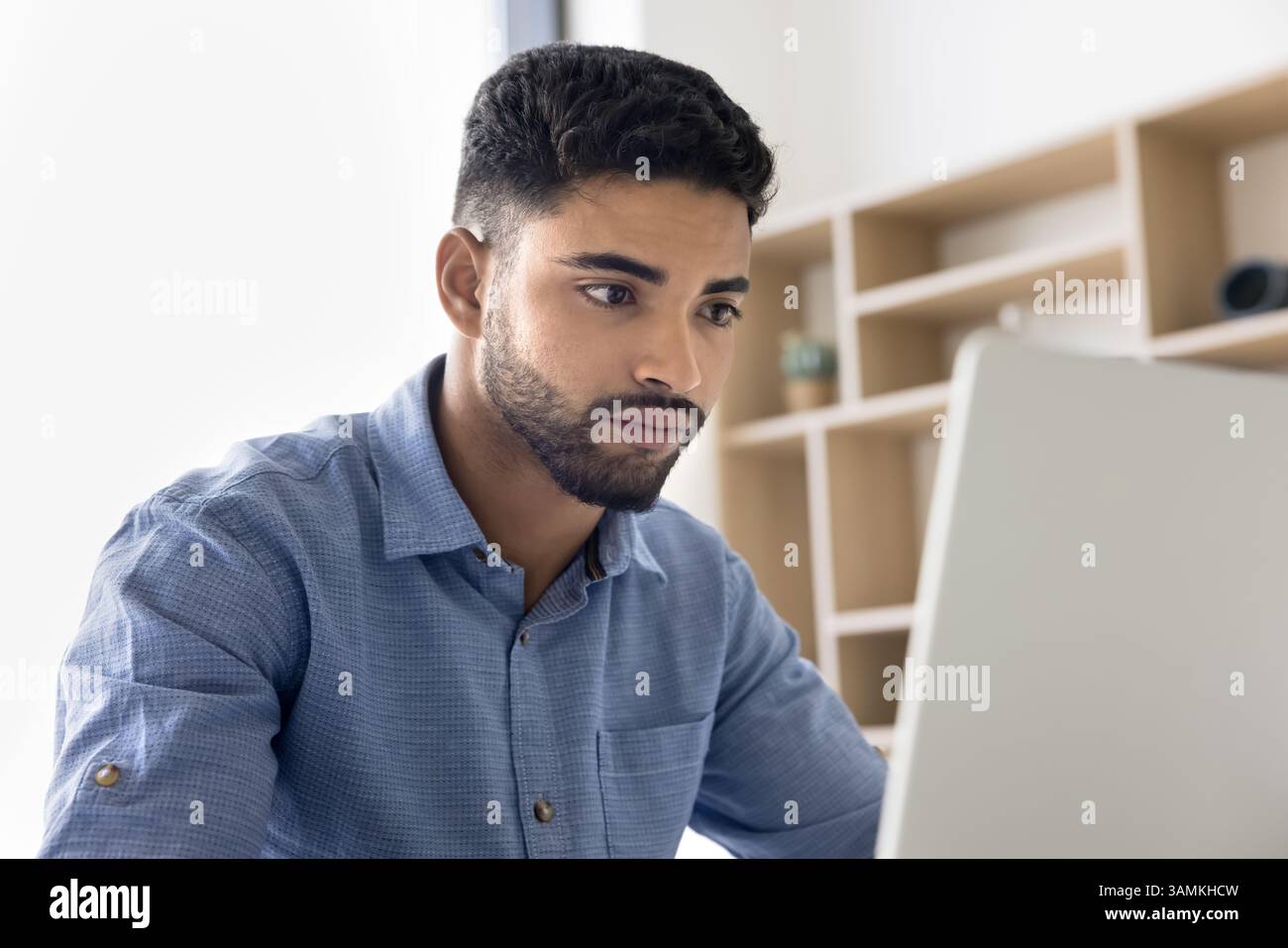 Concentrated young man looking at notebook screen taking exam remotely Stock Photo
