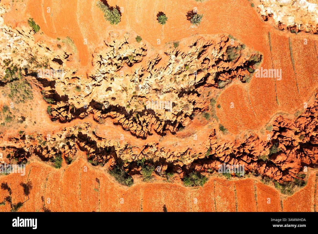 Aerial view of rugged rock formations and vibrant red earth with contrasting shadows and sparse vegetation, Southern Nations Nationalities and Peoples Stock Photo