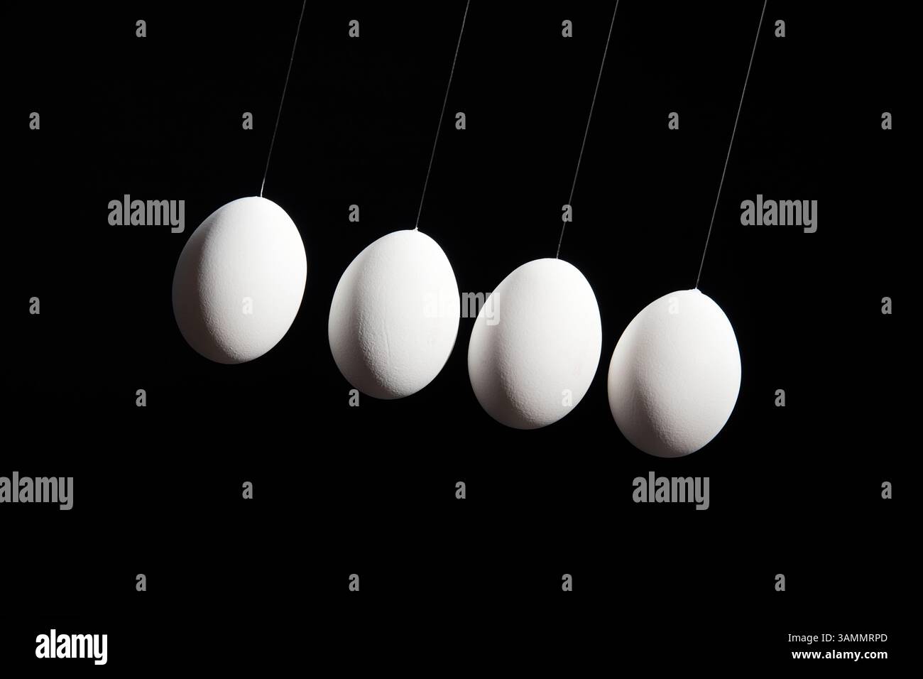 Four white eggs hang in a diagonal line against a deep black background, dramatically lit from the upper left corner. Front view. Stock Photo