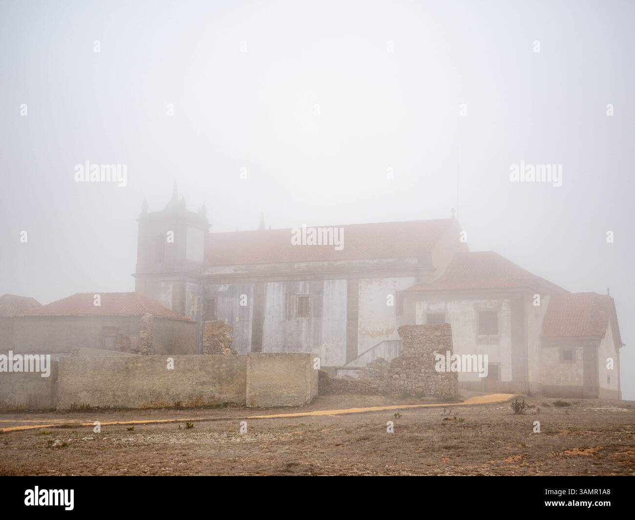 A captivating and mysterious coastal scene of the Cape Espichel Lighthouse shrouded in dense fog, standing tall against the gray, misty backdrop. The Stock Photo