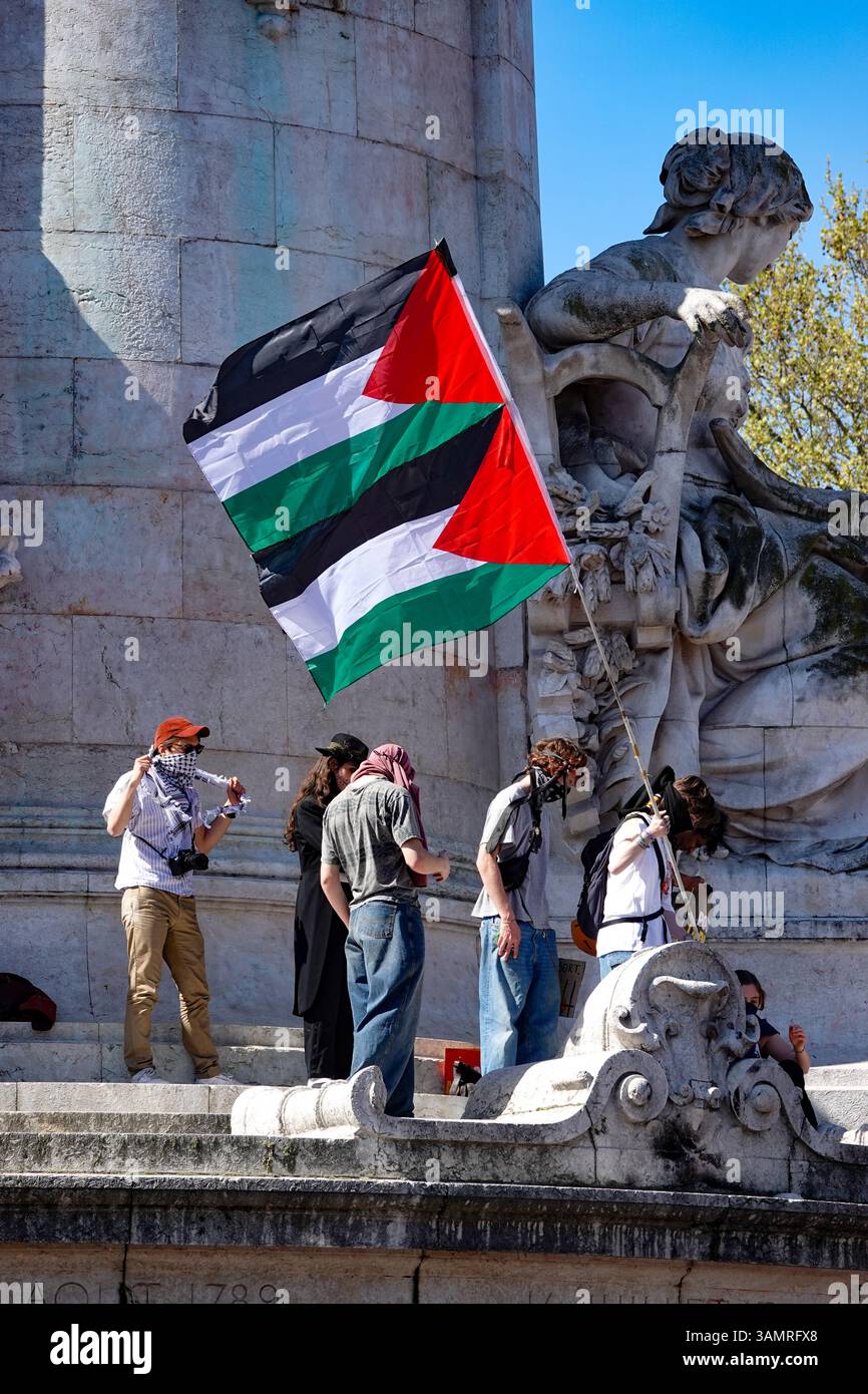 Pro-Palestine protesters wave a Palestinian flag in front of a monument at Place de la République, Paris, during a protest supporting Gaza. Stock Photo