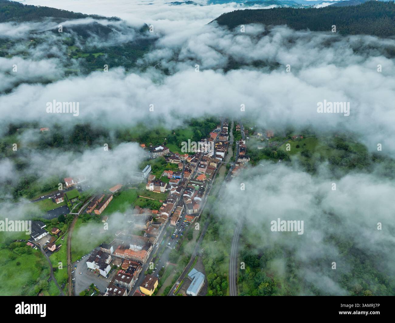 Aerial view of foggy village nestled in green hills with mist-covered ...