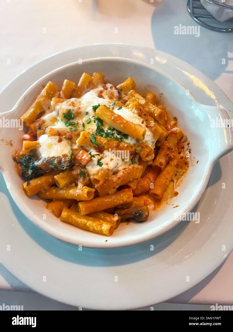 A comforting bowl of baked ziti topped with rich tomato cream sauce, melted mozzarella, and fresh herbs, served piping hot and ready to enjoy. - Smartphone Captured Stock Image