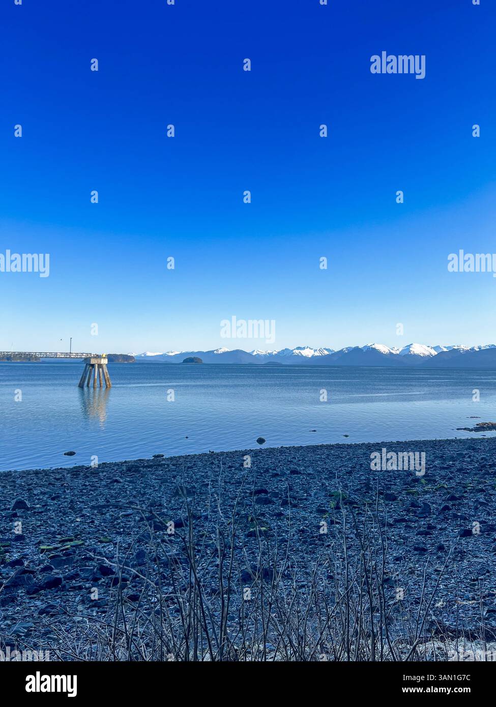 A crisp, clear view of Alaska’s coastal mountains and calm waters from the rocky shoreline. - Smartphone Captured Stock Image