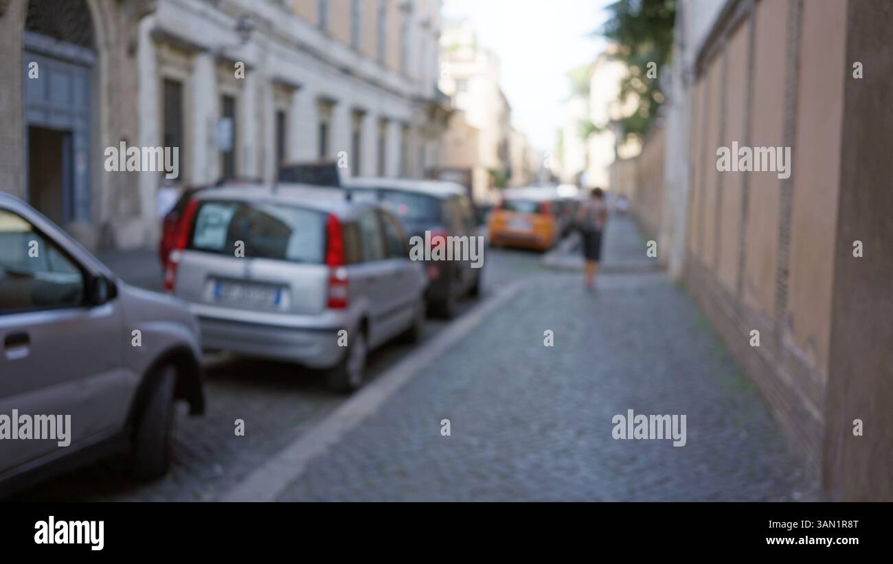 Blurred scene on a cobblestone street in rome with defocused cars and a ...