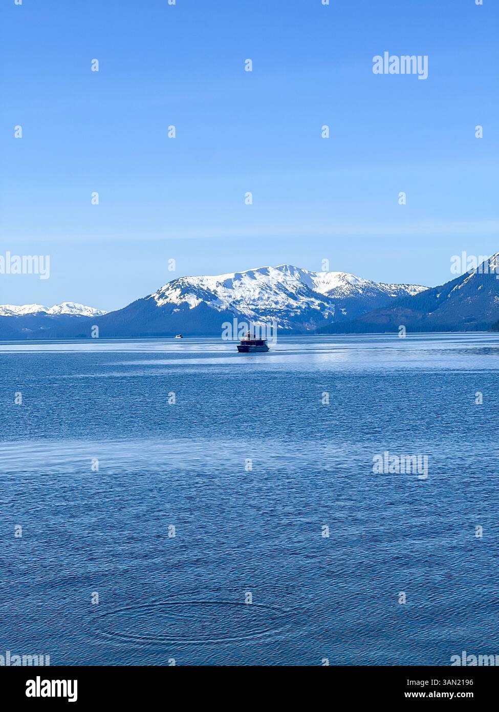 A peaceful boat drifts across the calm waters, framed by majestic snow-capped mountains. A breathtaking moment of serenity in the great outdoors. - Smartphone Captured Stock Image