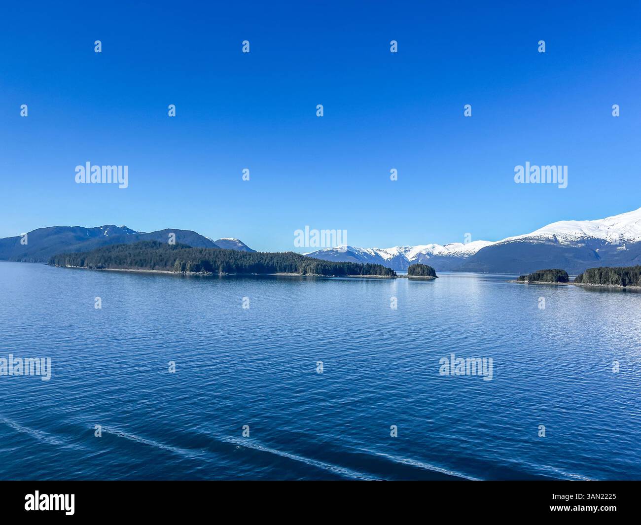A stunning view of snow-covered peaks and forested islands surrounded by deep blue waters. A perfect blend of serenity and untouched natural beauty. - Smartphone Captured Stock Image