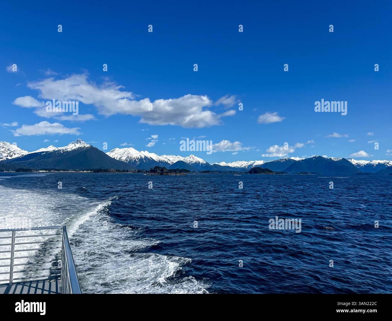 A stunning view from a boat as it moves through deep blue waters, leaving a trail of white foam with snow-capped mountains in the distance. A breathta - Smartphone Captured Stock Image