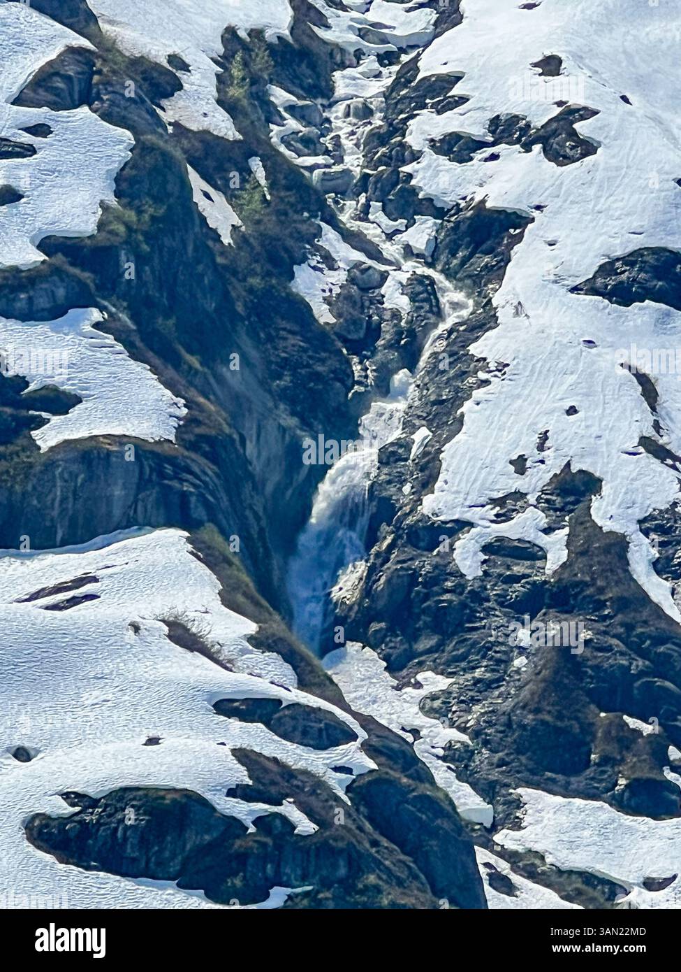A stunning waterfall flows through a rugged mountain pass, cutting through the snow and ice. Nature's power and beauty on full display in an alpine wo - Smartphone Captured Stock Image