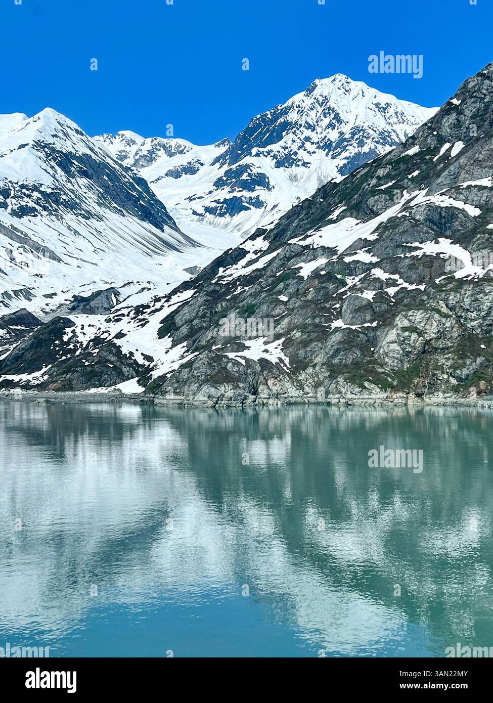 A stunning view of snow-covered mountains mirrored in the tranquil waters of Glacier Bay, Alaska. The perfect blend of rugged terrain and serene refle - Smartphone Captured Stock Image