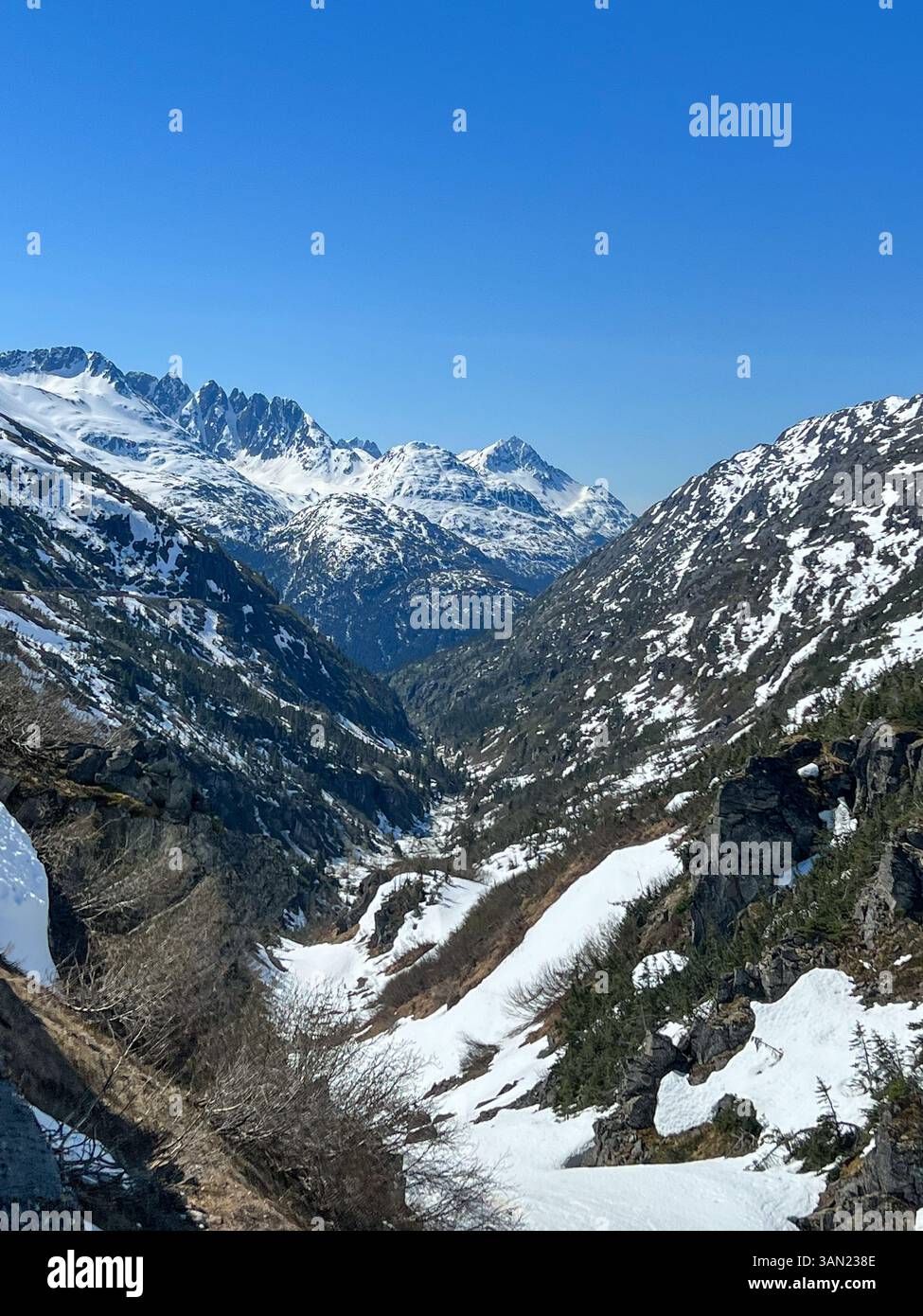 A breathtaking view of a snow-covered mountain valley in Alaska, surrounded by rugged peaks and deep valleys. The untouched wilderness and crisp blue - Smartphone Captured Stock Image
