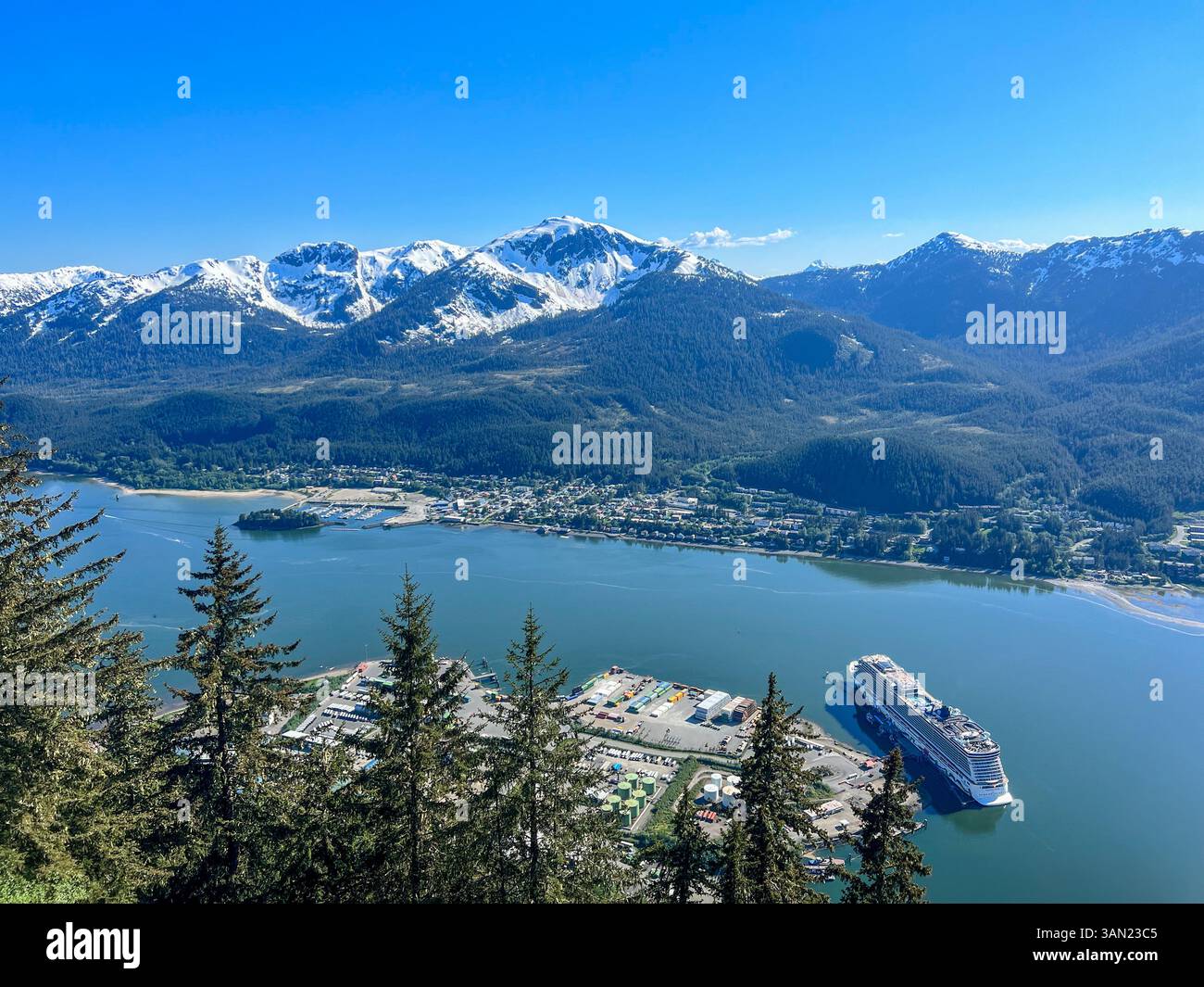 A stunning aerial view of Juneau, Alaska, showcasing its picturesque harbor, lush forested mountains, and a cruise ship docked at the port. The snow-c - Smartphone Captured Stock Image