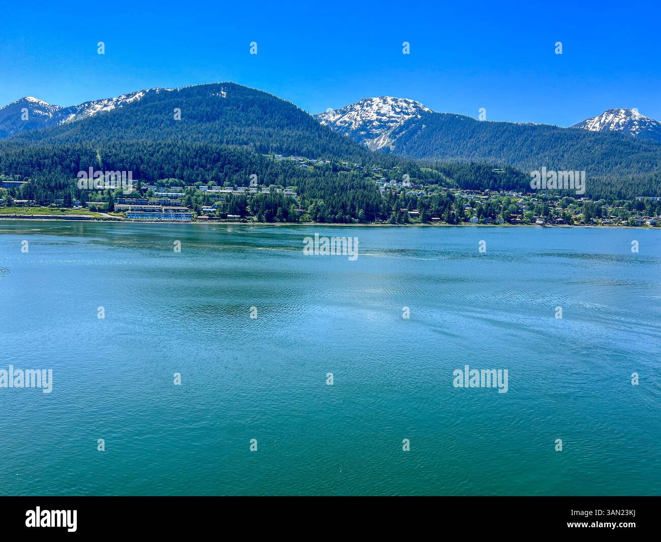 A serene view of Juneau, Alaska, featuring its calm waterfront, lush green forests, and snow-capped mountains in the background. This picturesque coas - Smartphone Captured Stock Image