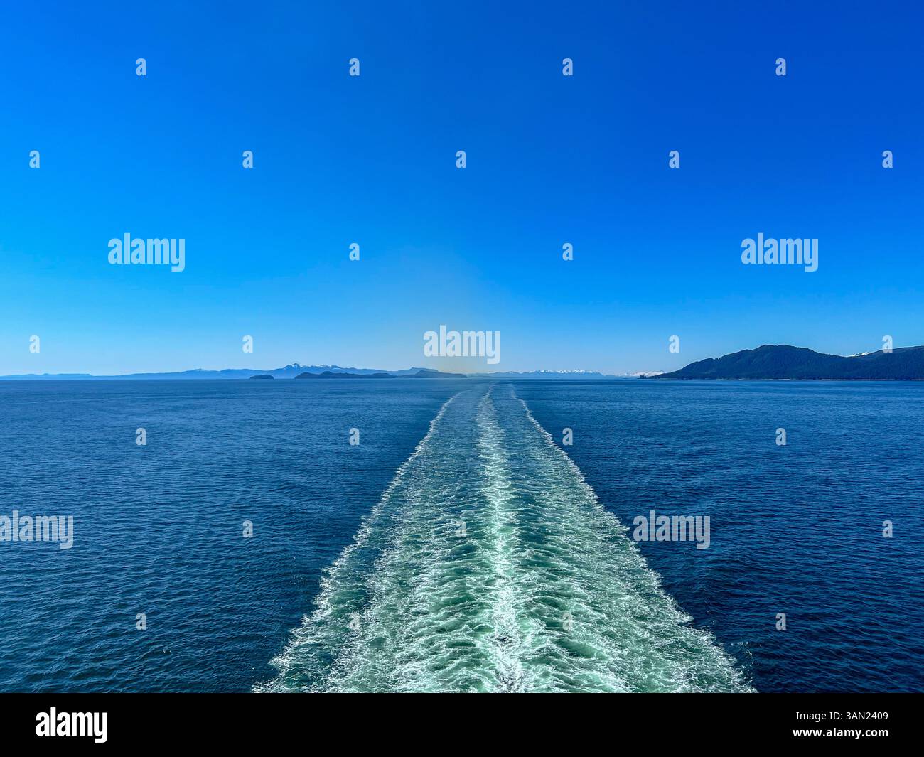 A stunning view of the open ocean as a cruise ship leaves a foamy wake behind. The vast blue waters stretch endlessly, with distant islands and snow-c - Smartphone Captured Stock Image
