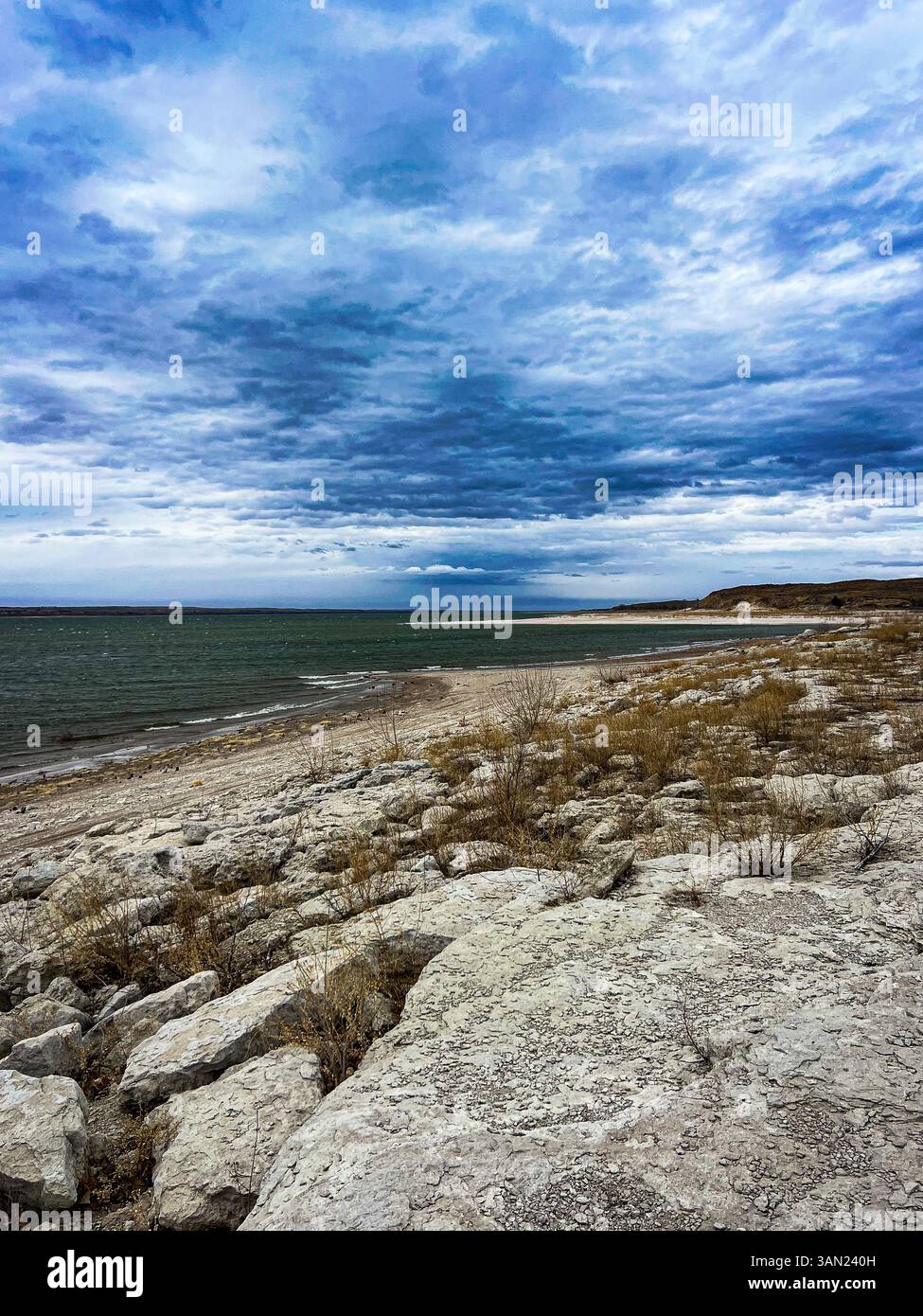 Waves roll gently onto the rocky shoreline as clouds gather overhead, setting a dramatic mood along this peaceful lakeside view. - Smartphone Captured Stock Image
