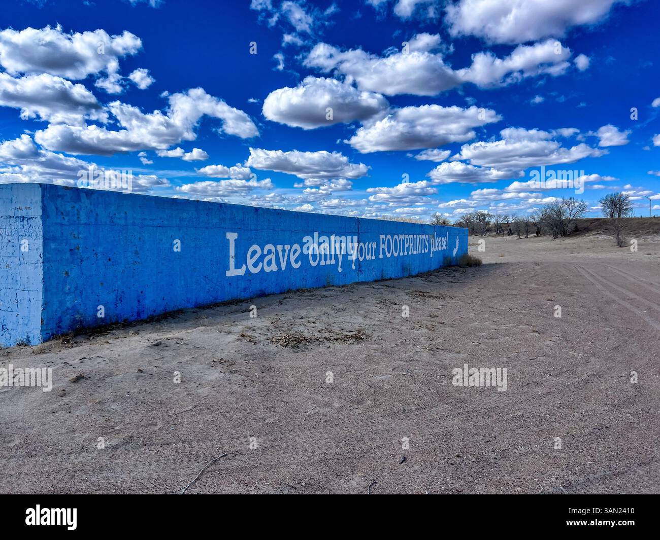 A simple reminder painted on a bright blue wall asks visitors to “Leave only your footprints” beneath a sky filled with cotton-like clouds. - Smartphone Captured Stock Image