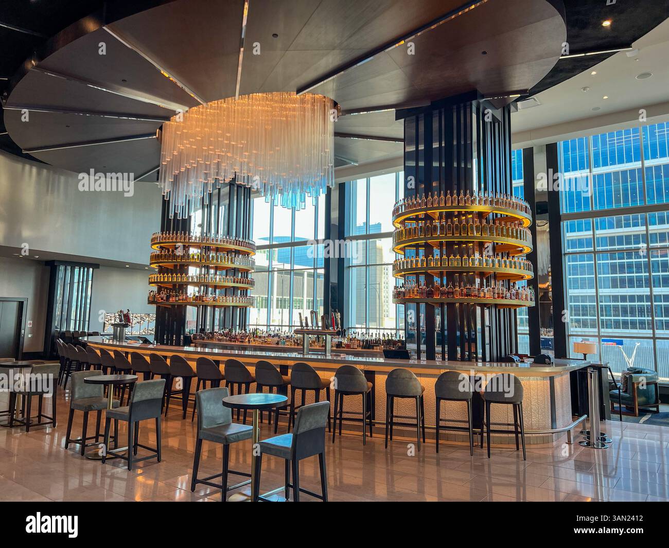 This sleek hotel bar features stunning spiral bottle displays and a dramatic chandelier, set against floor-to-ceiling windows overlooking the city sky - Smartphone Captured Stock Image