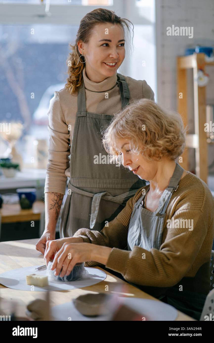 Teacher guides an elderly women, demonstrating sculpting techniques ...