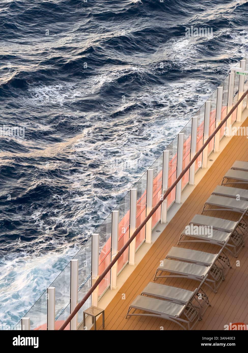 Sun loungers on cruise ship deck with sea and waves passing by, sunset - Smartphone Captured Stock Image