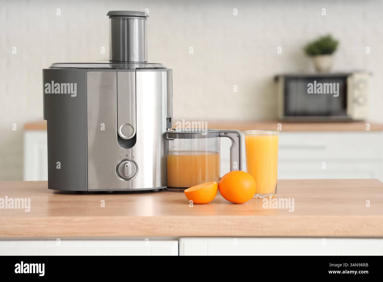 Modern juicer with fresh oranges on table in kitchen Stock Photo