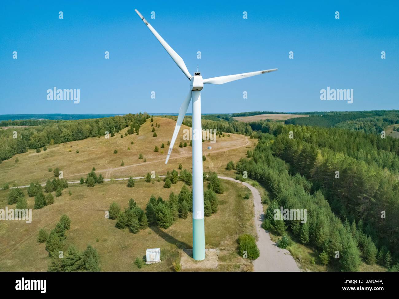 Tall wind turbine stands against a clear blue sky surrounded by green ...