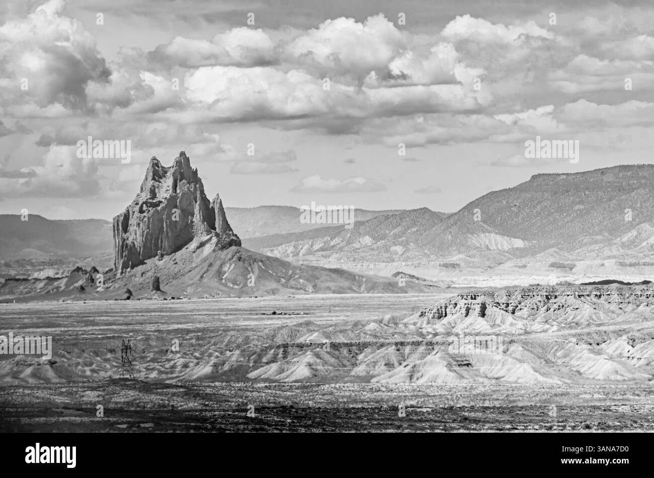 Black and white image of Shiprock in New Mexico rising from the desert landscape, with dramatic clouds and erosion patterns in the high desert. Stock Photo
