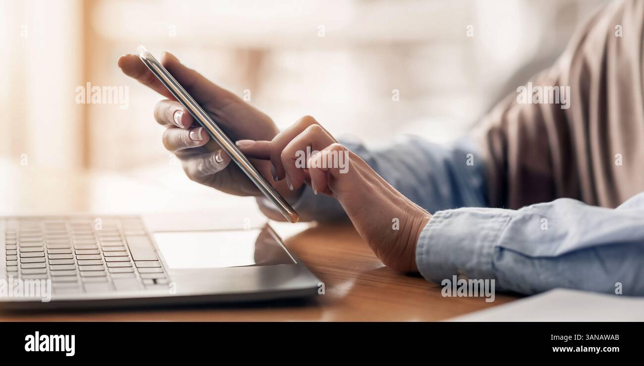 Female hands holding smartphone and using laptop Stock Photo