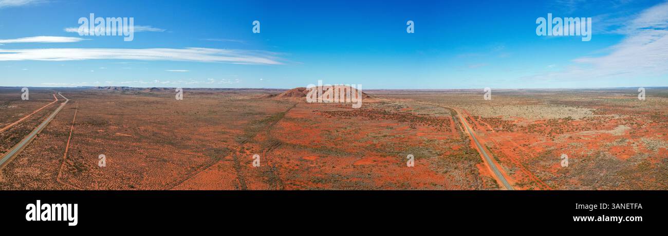 Aerial view of vast red earth and rugged landscape with distant mountains under a serene sky, Nanutarra, Western Australia. Stock Photo