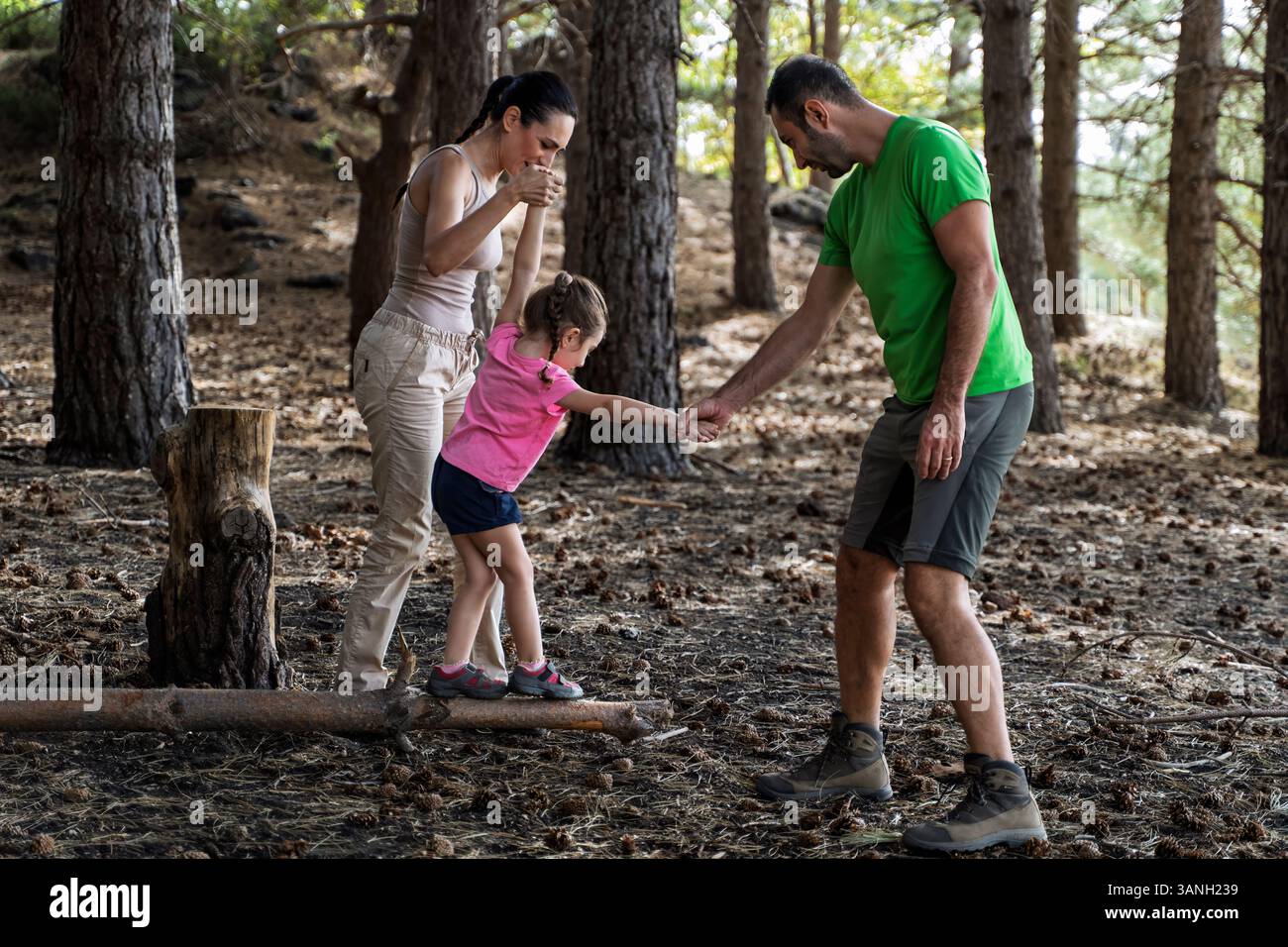 Parents helping daughter walk on a log during forest adventure ...