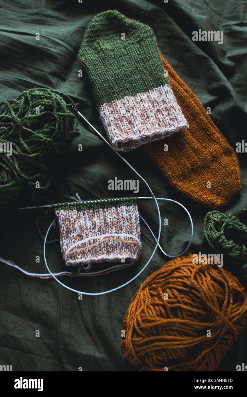 Dark green and brown yarn ball with knitted socks and knitting needles. Wool threads with deep green background. Woven crochet closeup. Knitting hobby Stock Photo