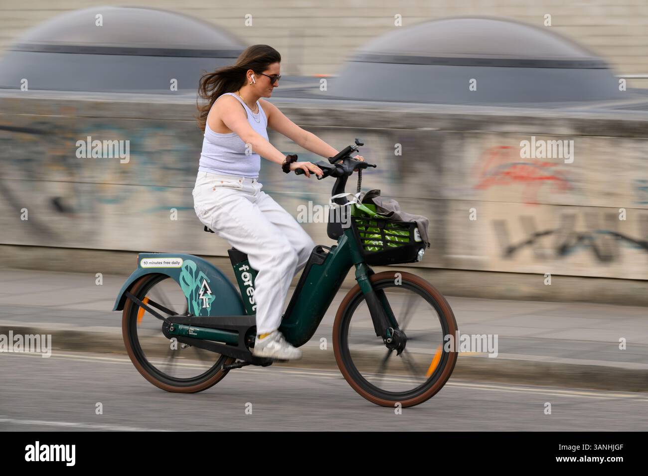 A woman ride on a Forest electric hire bicycle across Waterloo Bridge, London, UK.  12 Apr 2025 Stock Photo
