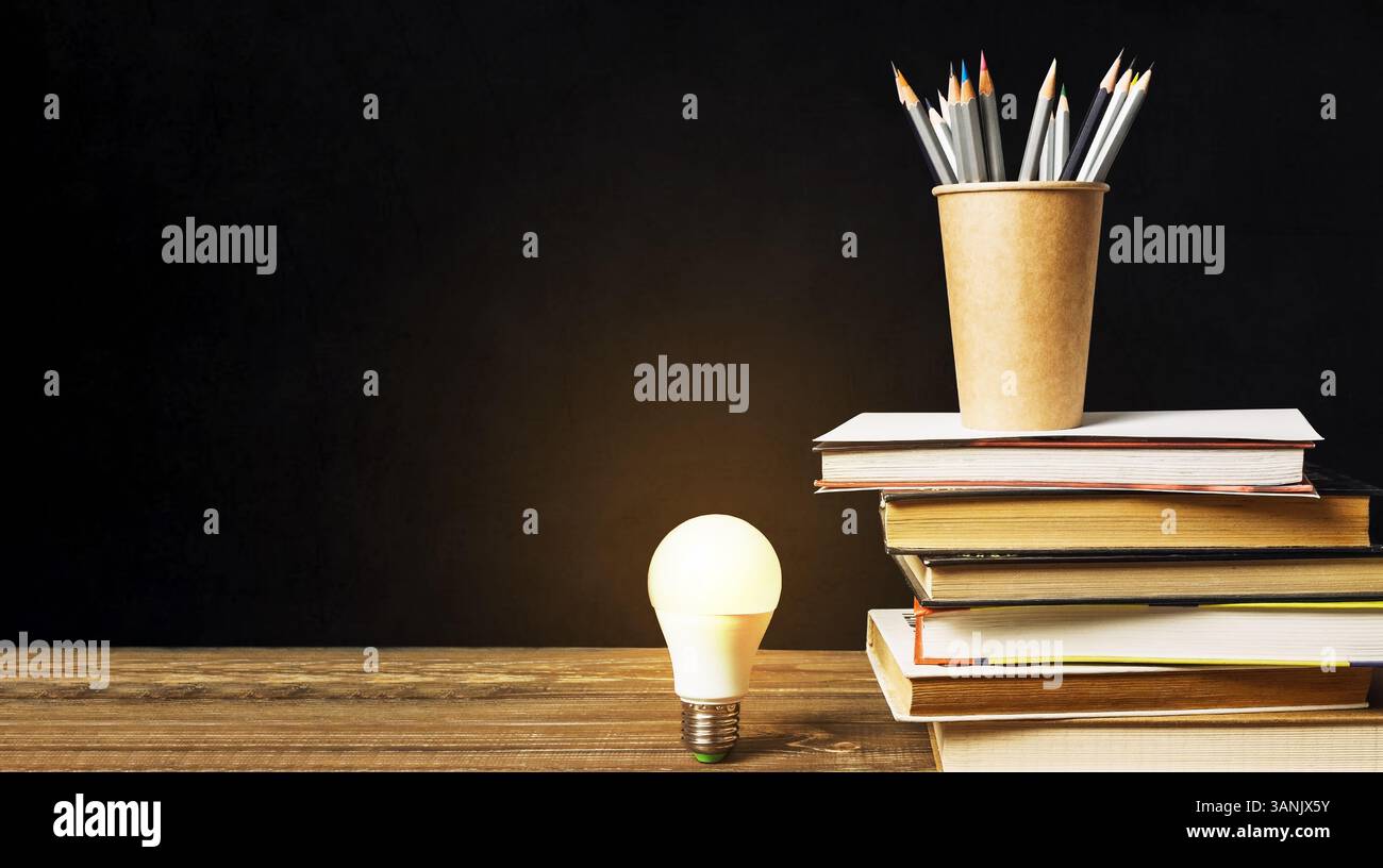 Light bulb is lit up on a table with a stack of books and pencils ...
