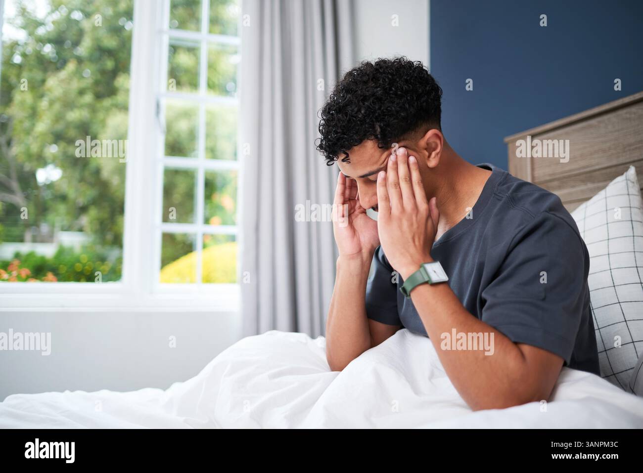 Man Sitting in Bed at Home Holding Head, Experiencing Discomfort Stock Photo