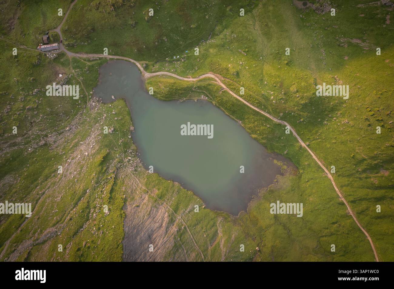 Aerial view of serene Lac Vert surrounded by majestic mountains and a winding road with a picturesque cottage, Val d'Illiez, Switzerland. Stock Photo