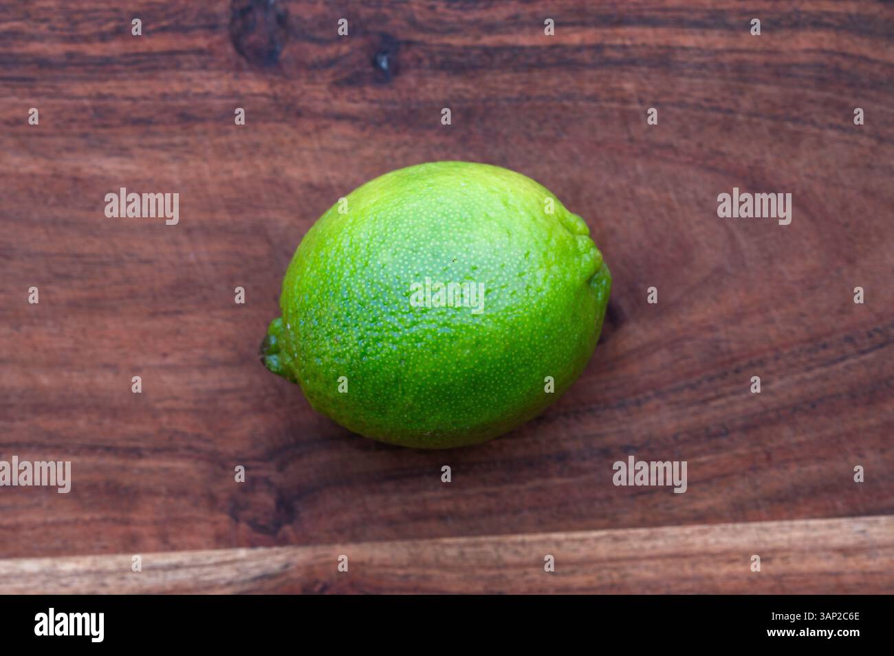 A whole green lime on a wood cutting board Stock Photo