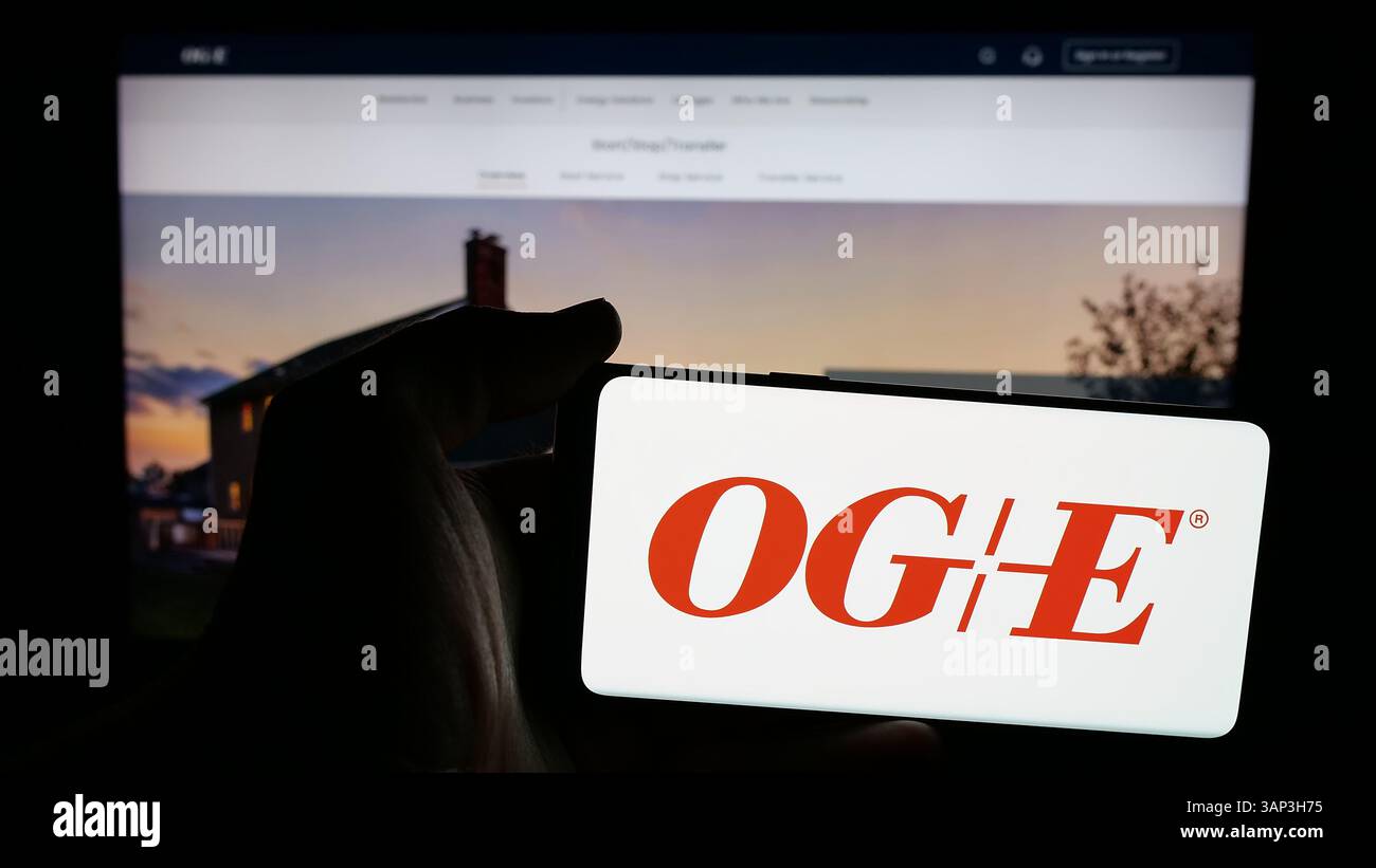 Stuttgart, Germany - 12-09-2024: Person holding mobile phone with logo of US company Oklahoma Gas Electric Company (OGE) on screen Stock Photo