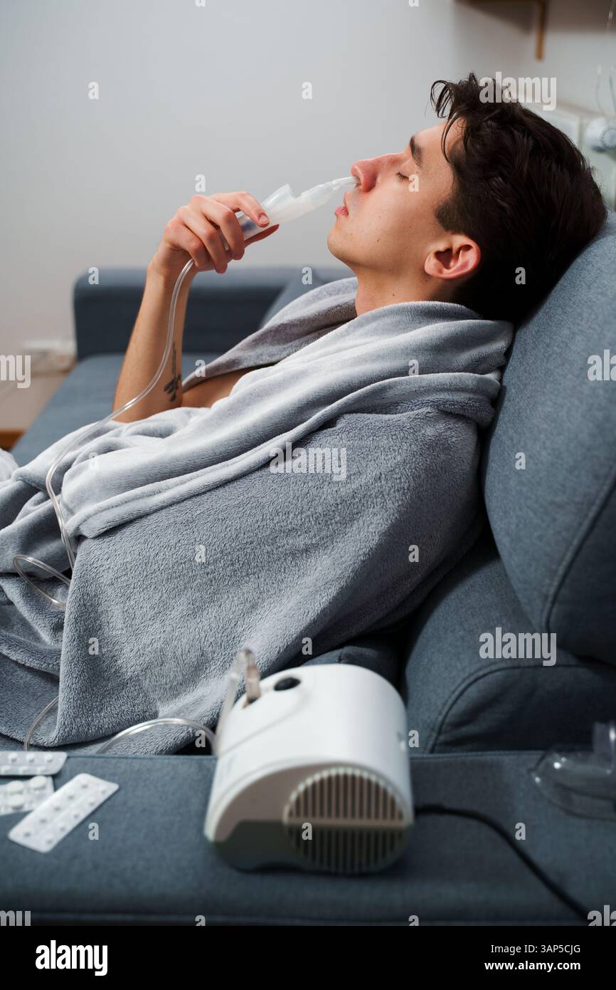 Young man with asthma attack breathing with inhaler in the bad. Doing ...