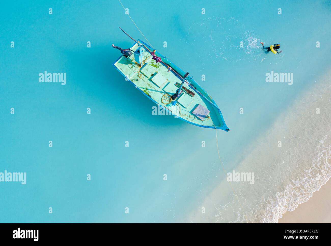 Aerial view of a blue fishing boat and a kid swimming in the lagoon, Maldives. Stock Photo