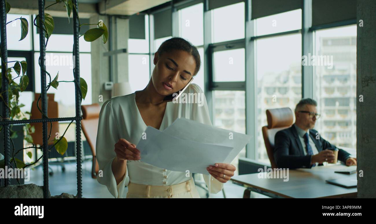 Businesswoman reads documents during phone call Stock Photo
