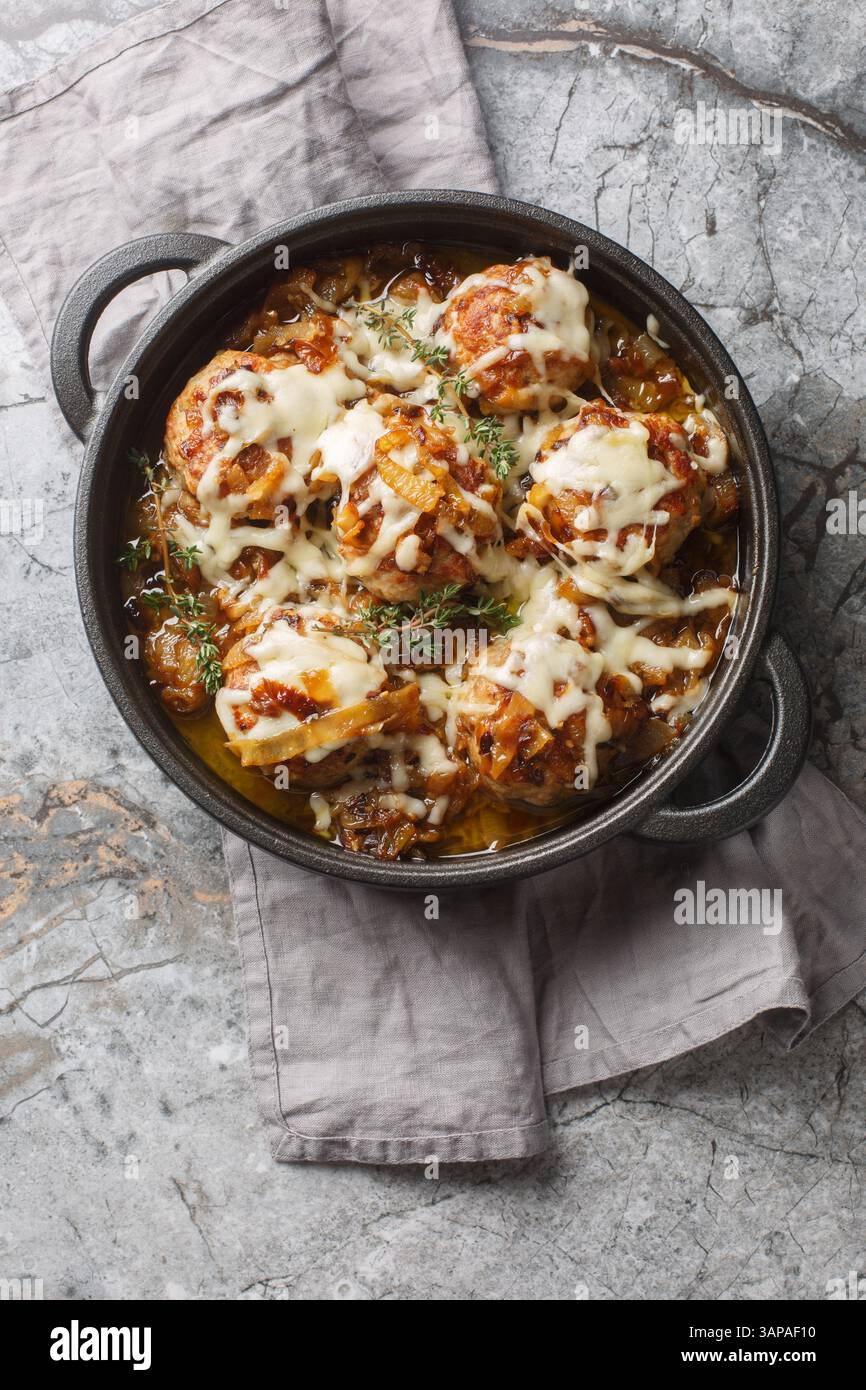 French onion meatballs are nestled into a rich, savory onion sauce and topped with Gruyere and mozzarella cheese closeup on the pan on the table. Vert Stock Photo