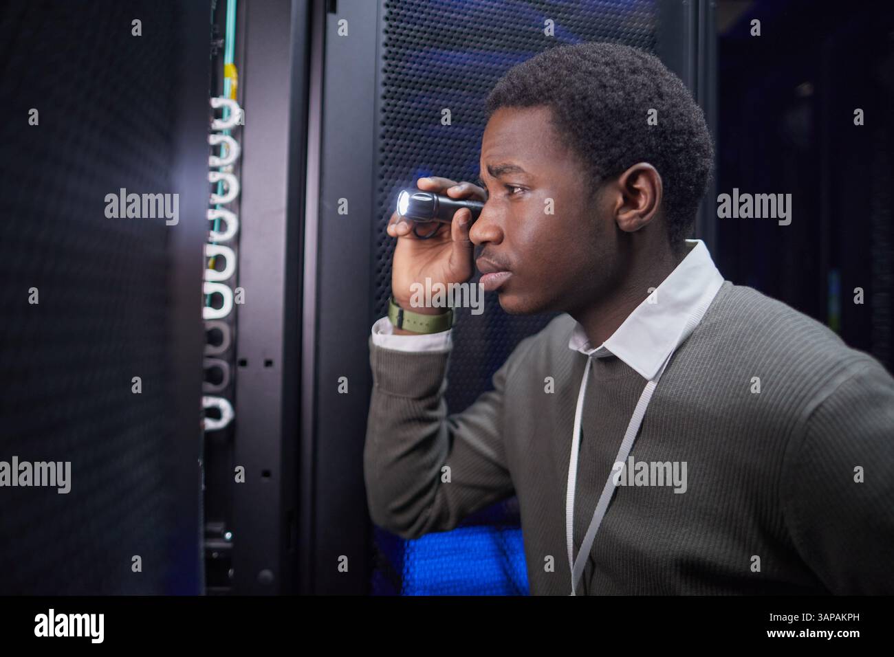 Focused IT technician inspecting server racks with flashlight while ensuring performance and security in modern data center environment Stock Photo